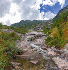 Panoramic view of a stream flowing on the steep rocky walls of Monte Rosa in Piedmont, Italy.