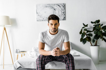 handsome confident man in pajamas sitting on bed at home