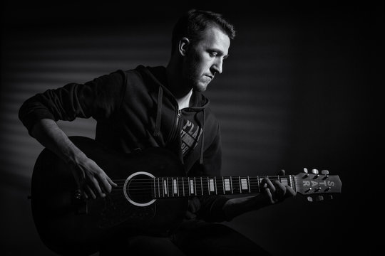 Young man playing acoustic guitar on dark background.