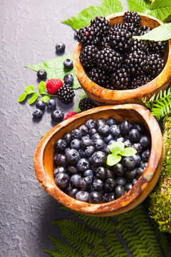 Freshly assorted berries in wooden bowl. Juicy and fresh blueberries6 blackberries and raspberries with green leaves on rustic background. Concept for healthy eating and nutrition.