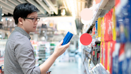 Asian man shopper choosing fizzy drink or carbonated soft drink in can package from shelf in supermarket or grocery store. Shopping sugary product. Unhealthy lifestyle.