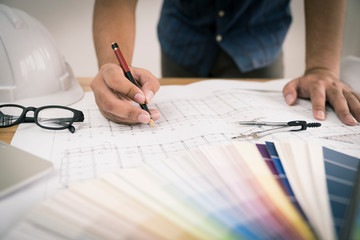 architect or civil engineer during drawing home or building in office on working table with office stationary , laptop ,color pallette sampling.drawing is fake only for stock photo.