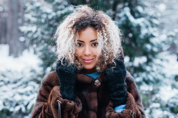 Fototapeta premium Close-up portrait of beautiful young afro american woman in snow winter forest
