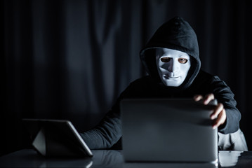 Mystery male hoodie hacker holding white mask looking at laptop computer. Anonymous social masking....