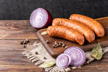 Smoked sausage with spices and onion on wooden background.