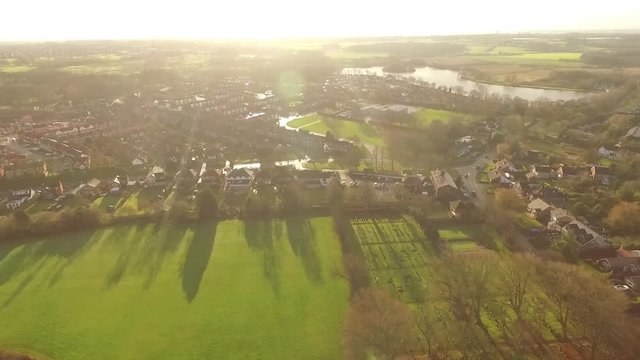 Aerial views across UK, British, countryside town houses with views of lake & light leak countryside horizon.