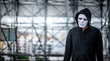 Mystery hoodie man in white mask standing in the rain on rooftop of abandoned building. Bipolar disorder or Major depressive disorder. Depression concept