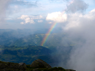 Rainbow between the land and clouds high in Carpathian Mountains.  Heaven kitchen prepares rainy whether in mountains. Picturesque mountain scenery. Eastern Carpathians, Ukraine