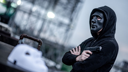 Fototapeta na wymiar Mystery hoodie man in broken black mask holding gun feeling guilty. Crime and violence concepts