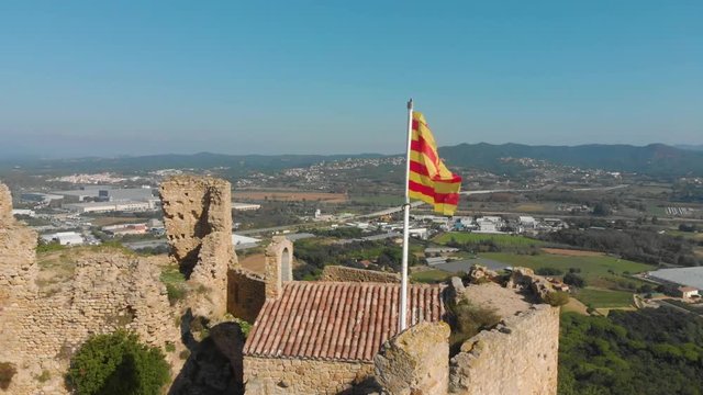 Detail of Catalonia flag fluttering and hoisted in castle Palafolls Castle ruins on a sunny day. Catalonia Spain. Aerial view travelling orbit