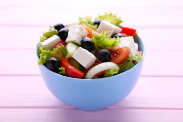Fresh greek salad in bowl on pink wooden background