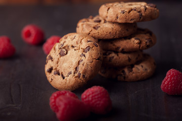 Chocolate chip cookies on dark old wooden table with red raspberry. Tasty snack.