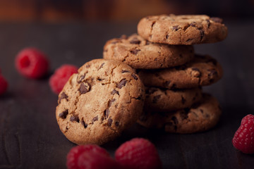Fototapeta na wymiar Chocolate chip cookies on dark old wooden table with red raspberry. Tasty snack.