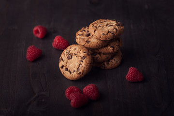 Chocolate chip cookies on dark old wooden table with red raspberry. Tasty snack.