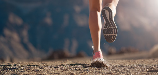 Running shoe closeup of a woman running on a gravel path with sports shoes in a mountain environment - obrazy, fototapety, plakaty