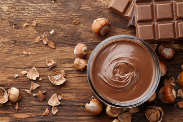 Chocolate spread with hazelnuts on wooden background