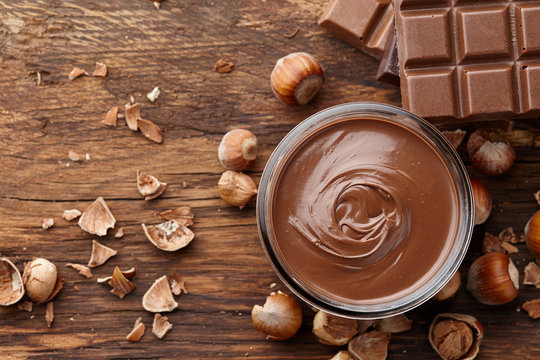 Chocolate spread with hazelnuts on wooden background