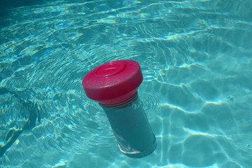 Close up of a floating swimming pool chlorine dispenser in sparkling clean water.
