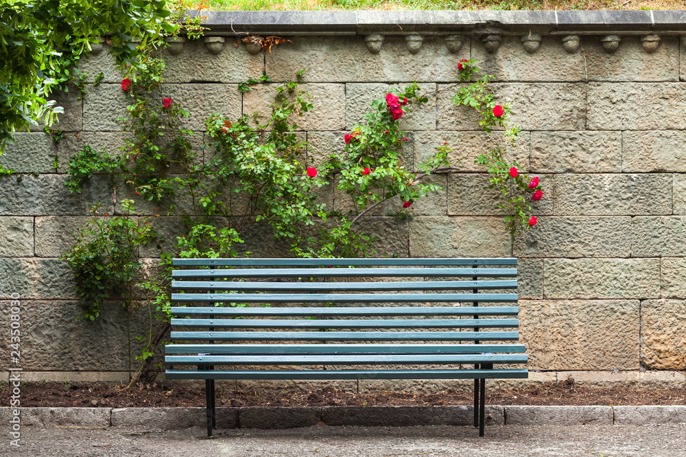 Wall mural Empty blue wooden bench stands near stone wall