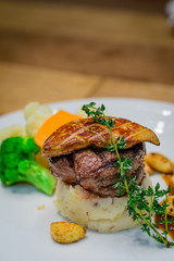 Grilled tenderloin filet mignon medallion with bacon mashed potatoes & seasonal vegetables.  Topped with foie gras and served with red wine garlic confit sauce.