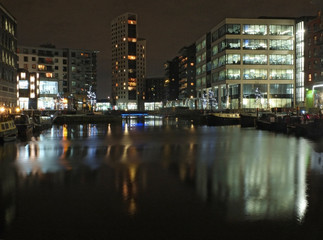 Fototapeta na wymiar clarence dock in leeds at night with brightly illuminated buildings reflected in the water and boats moored along the sides