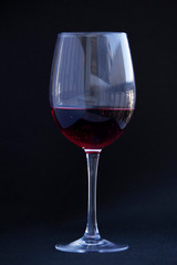 Crystal clear wine glass with traditional round goblet shape filled with dark red wine.