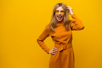 Excited young woman in orange dress, widely smiling, looking at camera. Isolated on yellow...