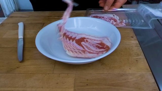 Chef cuts the raw bacon into a white dish to fry it in extra-virgin olive oil