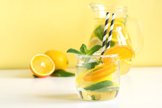 Summer refreshing cocktail with lemon, orange, mint and ice in glass on yellow. Summer detox drinks.