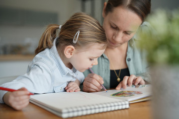 Fototapeta na wymiar Mother and young daughter drawing and reading together at home