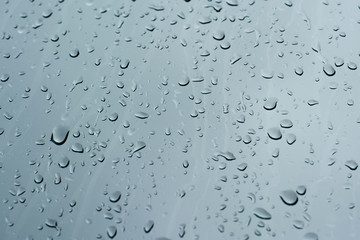 Rain drops on a window glass surface against a dark background of stormy sky.