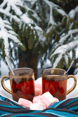 Two cups of tea with marshmallows under the tree in winter in the snow