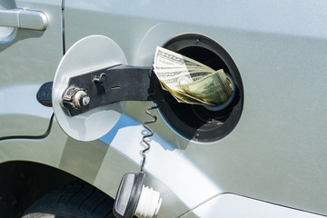 Fuel tank of a silver car filled with US dollar banknotes, symbolizing high cost of fuel