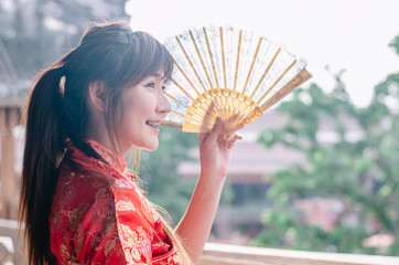 Portrait beautiful young woman smile wear cheongsam deep red dress holding a fan looking outside. Festivities and Celebration concept
