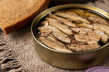 Sprats in tin can and bread on dark wooden background.