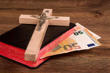 Crucifix on the background of the book with euro banknotes