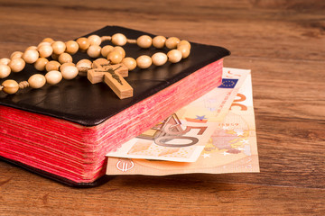 Rosary on the background of the book with euro banknotes
