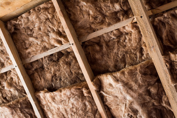 Glass wool in a wooden frame on a inclined wall near the wooden ceiling in a private house. Warming...