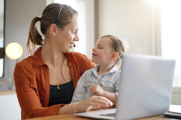 Mother working from home on computer with her young daughter