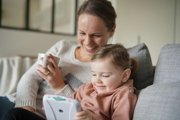 Mother and young daughter playing games on child's tablet at home