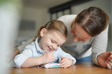 Mother and daughter having fun playing with child's tablet at home