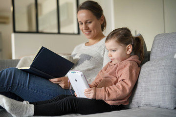 Mother and young daughter reading and playing on tablet at home