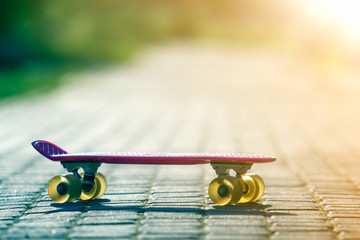 Close-up of child plastic pink skateboard isolated on pavement against bright white and green...
