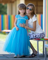 Young slim blond smiling mother, aunt or sister hugs small pretty preschool daughter girl in long...