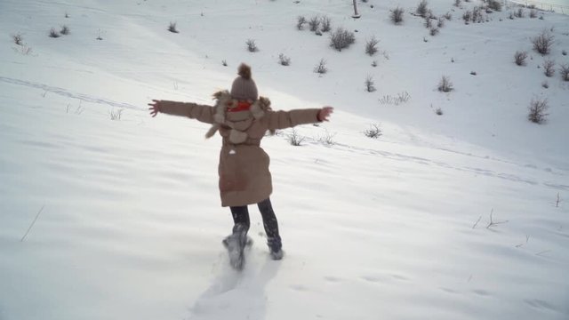 Young beautiful girl runs on the snow and jumps into it and starts making a snow angel. Slow motion video 100p