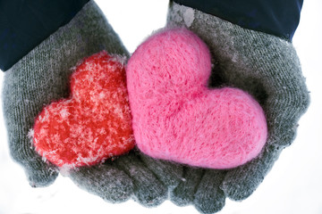 Hands in wollen gloves holding two woolen hearts covered with snowflakes isolated on white