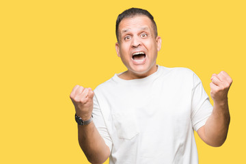 Middle age arab man wearig white t-shirt over isolated background celebrating surprised and amazed for success with arms raised and open eyes. Winner concept.