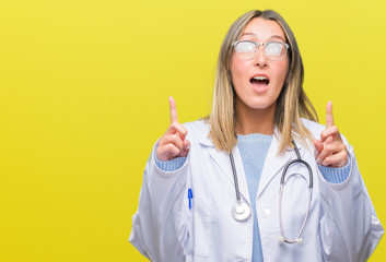 Young beautiful doctor woman headphones over isolated background amazed and surprised looking up and pointing with fingers and raised arms.