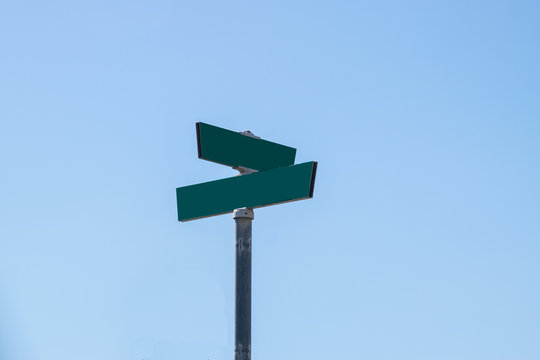 Blank green street signs on metal post with blue sky background