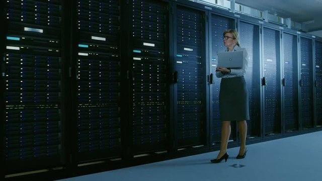 In Data Center Female IT Specialist Walks along the Row of Operational Server Racks, Checking Normal Functioning. Modern High-Tech Telecommunications Operational Data Center.